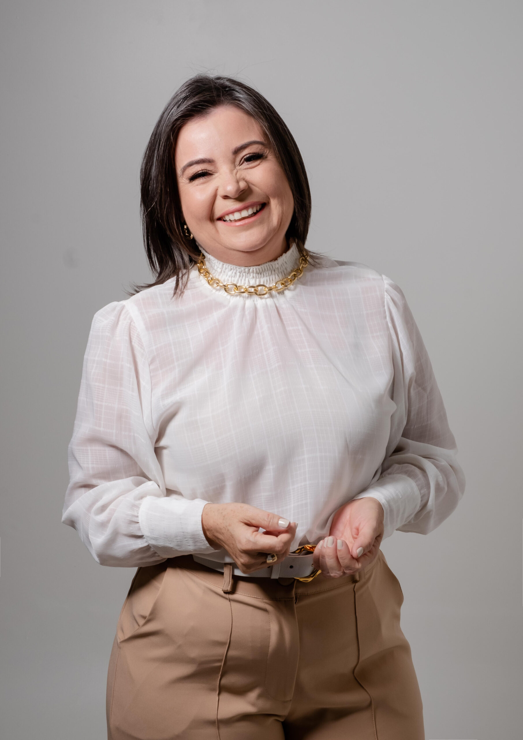 Psicóloga sorrindo com um colar de ouro em volta do pescoço. Blusa branca.